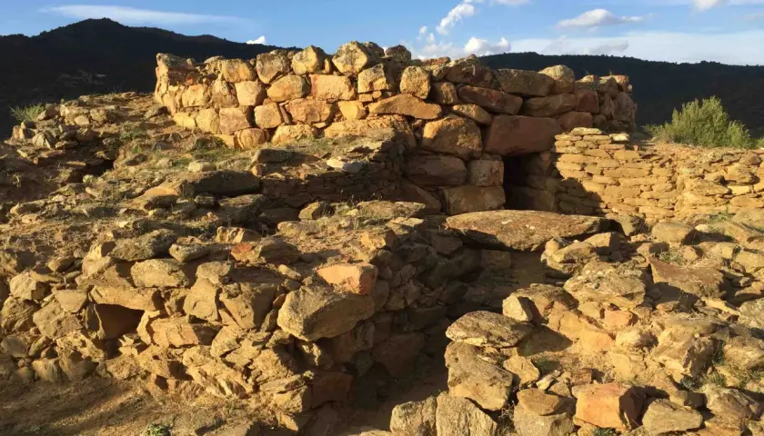 Rovine del nuraghe San Pietro, una struttura in pietra con un ingresso scuro, sotto un cielo azzurro con nuvole bianche.