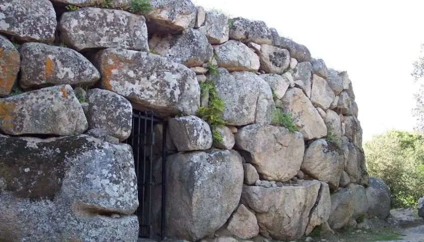 Muro imponente di un nuraghe, con un cancello in ferro che custodisce l'ingresso. Le pietre antiche, segnate dal tempo, raccontano storie millenarie.