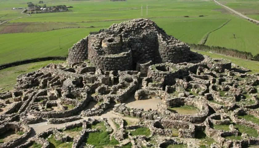 Antica fortezza nuragica in pietra, con torri e mura a vista, immersa in un paesaggio rurale verdeggiante. I nuraghi dove si trovano sono testimoni di un passato millenario.