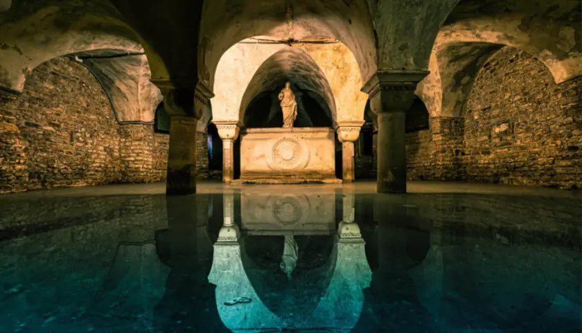 La cripta di San Marco, con le sue volte in pietra e la statua riflessa sull'acqua, evoca un'atmosfera mistica e antica.