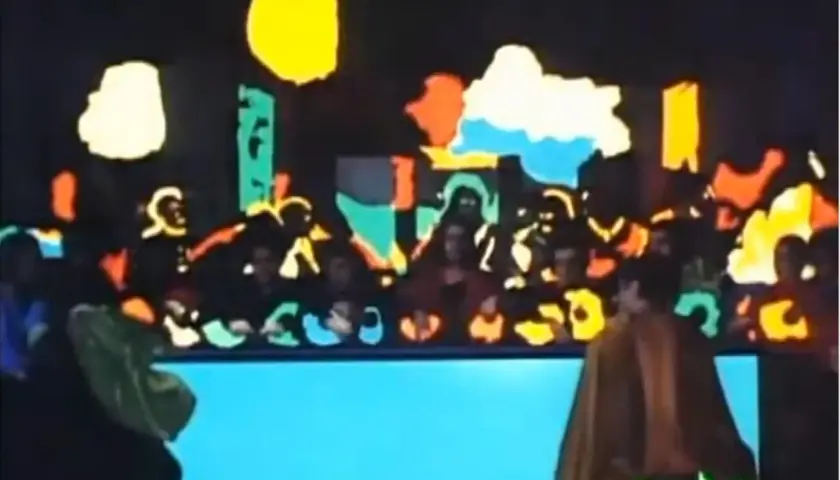 Scena colorata con figure stilizzate, forse una rappresentazione teatrale. Si intravede un personaggio con un mantello marrone, forse **Salomé**, bene in vista.