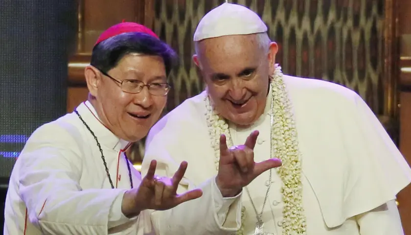 Papa Francesco e un vescovo fanno il gesto delle corna a tre dita, un segno di benedizione e speranza.