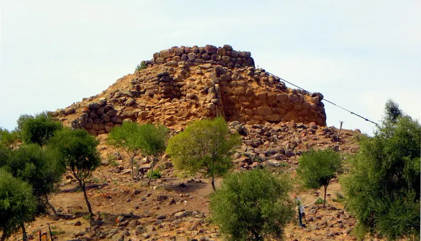 Il nuraghe Sirai, imponente struttura in pietra, si erge su un colle arido, circondato da vegetazione mediterranea.
