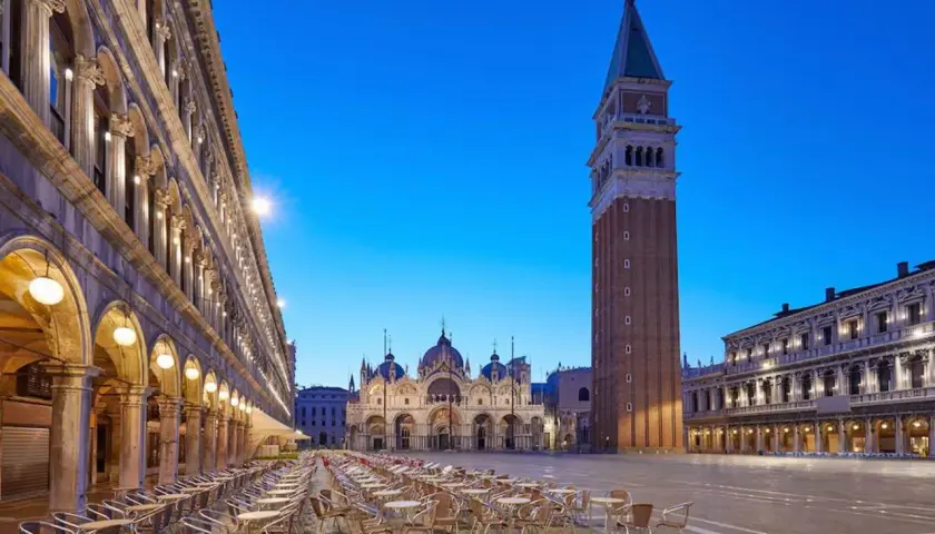 Un maestoso palazzo in Piazza San Marco, Venezia, si erge con la sua architettura imponente, mentre il cielo azzurro della sera fa da sfondo.