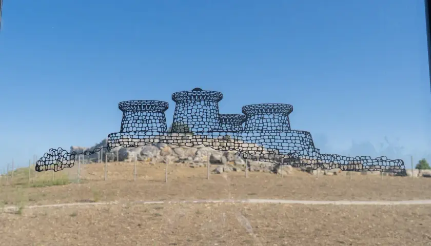 Disegno stilizzato del nuraghe Genna Maria, con torri tronche e mura merlate, su uno sfondo di cielo azzurro e terreno brullo.