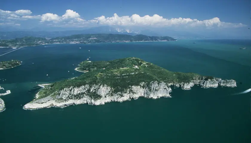 Isola verdeggiante con scogliere bianche, mare blu intenso e nuvole bianche. Si intravede la **grotta dei colombi** tra le rocce.