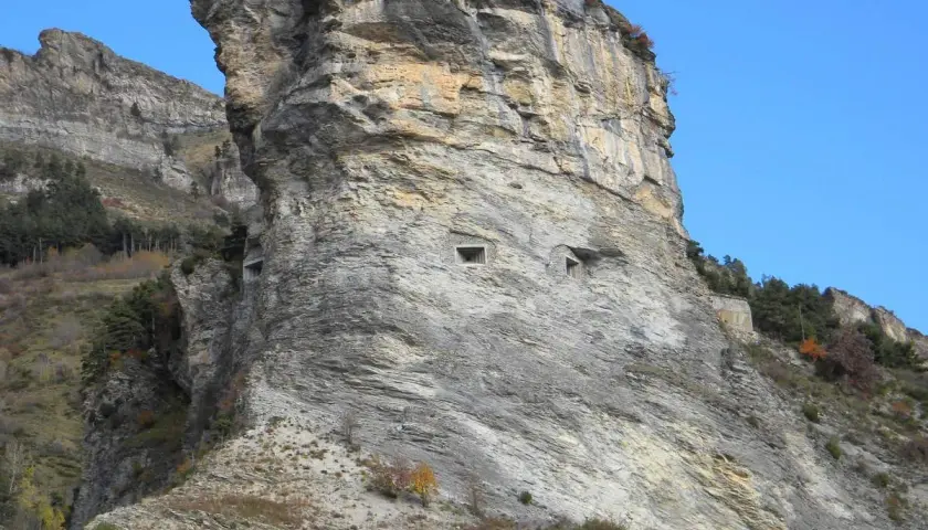 Imponente roccia con aperture che ricordano il vallo alpino del littorio. Un paesaggio montano suggestivo sotto un cielo azzurro.