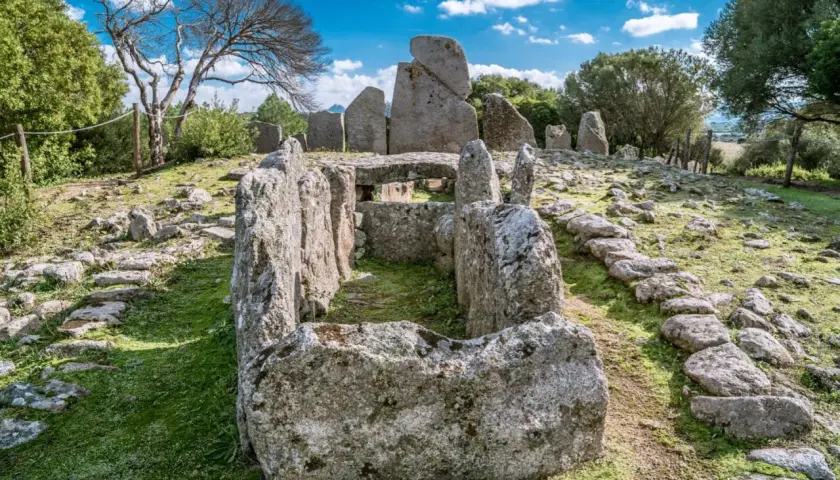Antica tomba dei giganti di Li Lolghi, con imponenti pietre erette e un corridoio centrale, immersa nel verde sotto un cielo azzurro.