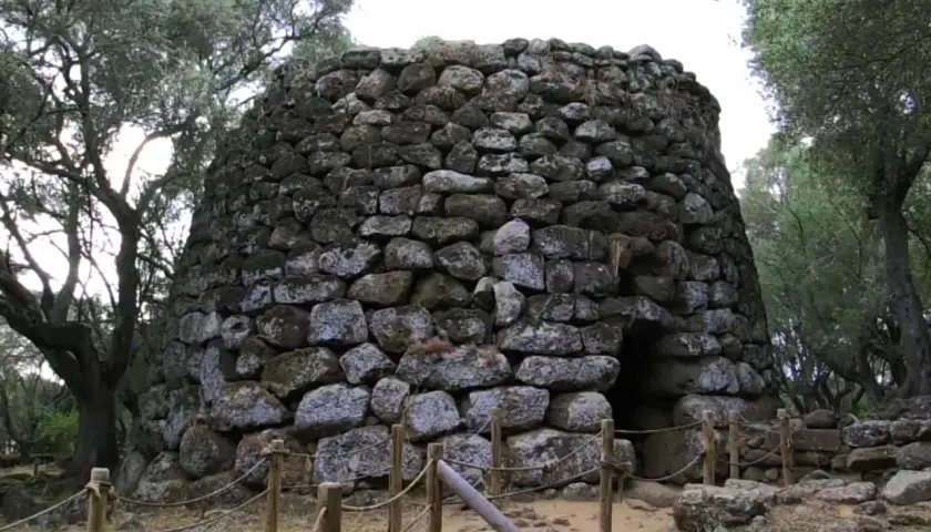Antico nuraghe di Santa Cristina a Paulilatino, imponente struttura in pietra con un ingresso buio, circondato da alberi secolari.