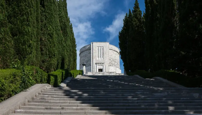 Lunga scalinata conduce all'imponente ossario di Oslavia, fiancheggiata da alti cipressi e vegetazione curata.