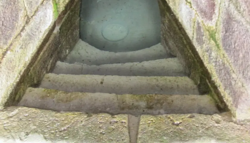 Antica scala in pietra conduce a un pozzo sacro in Sardegna, le cui acque limpide riflettono il cielo.