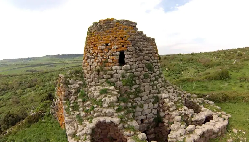 Il nuraghe Santa Barbara, con la sua torre in pietra ricoperta di licheni arancioni, domina un paesaggio verdeggiante e collinare.