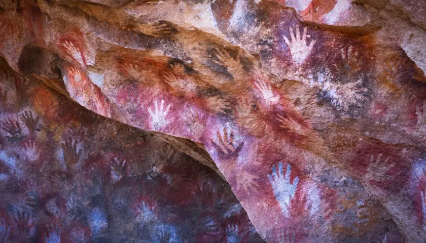 Antiche pitture rupestri nella grotta delle mani, con impronte di mani rosse e bianche su roccia.