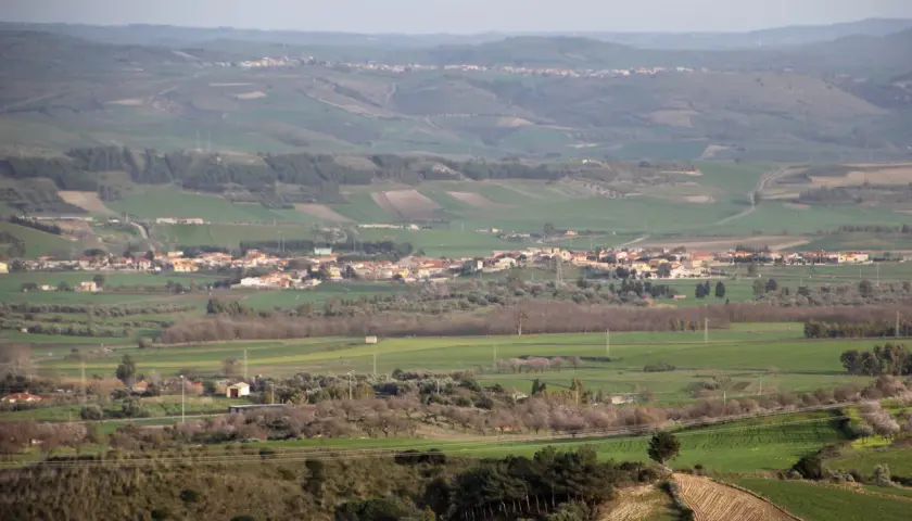 Paesaggio collinare con campi coltivati e case sparse, in lontananza si intravede il borgo di Pauli Arbarei, Sardegna.
