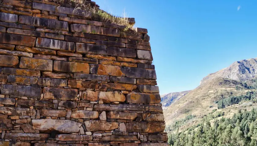 Antiche mura di pietra a Chavin de Huantar, con montagne verdi e cielo azzurro sullo sfondo.