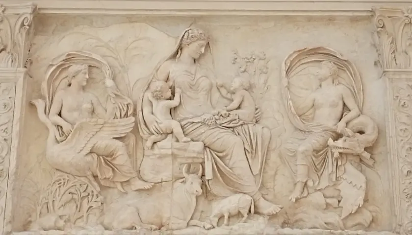 Rilievo esterno dell'Ara Pacis: una madre con due bambini, affiancata da figure femminili con cigno e creatura marina, circondata da animali e vegetazione.