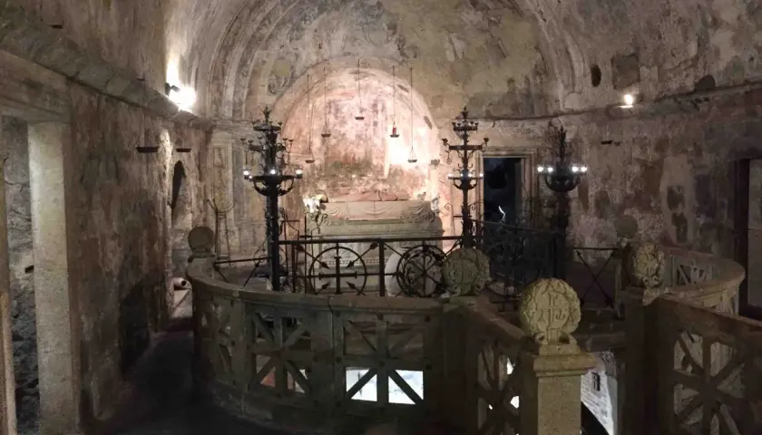 Interno della cripta di Santa Cristina, con affreschi antichi, candelabri e un sarcofago.