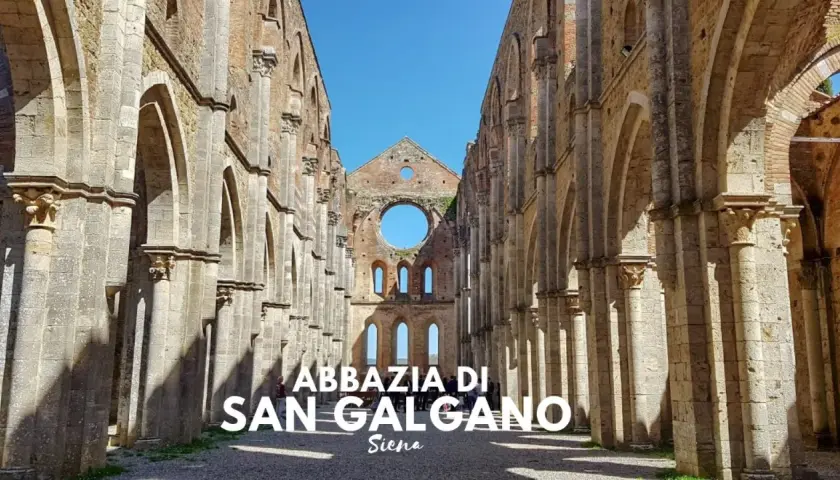 L'abbazia di San Galgano, un'imponente rovina nel cuore di un querceto, si erge maestosa sotto un cielo azzurro.