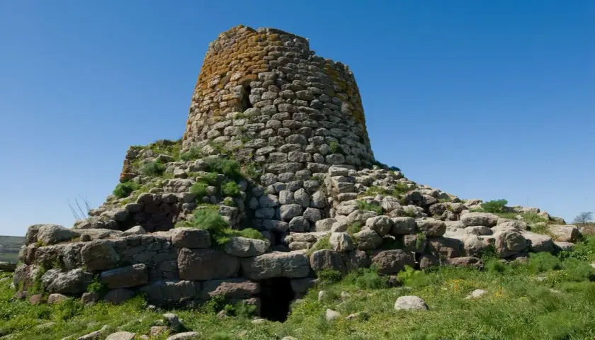 Il nuraghe Santa Barbara a Villanova Truschedu, imponente struttura in pietra con vegetazione rigogliosa, si erge sotto un cielo azzurro.