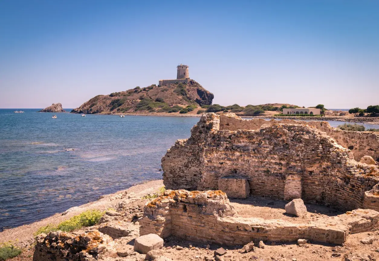 Rovine antiche sulla costa sarda, con una torre in lontananza. Un pezzo di storia della Sardegna che emerge dal passato.