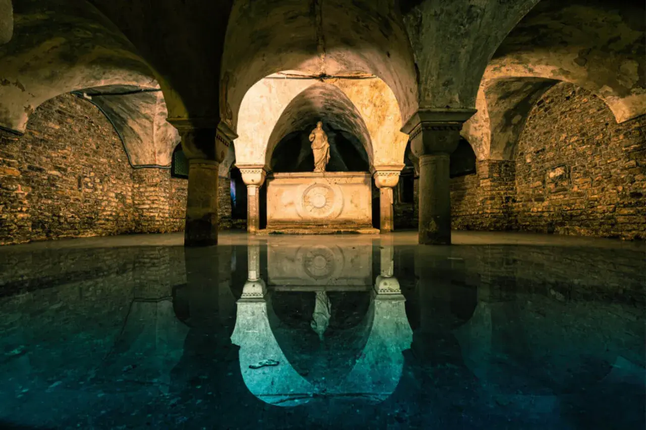 La cripta di San Marco, con le sue volte in pietra e la statua riflessa sull'acqua, evoca un'atmosfera mistica e antica.