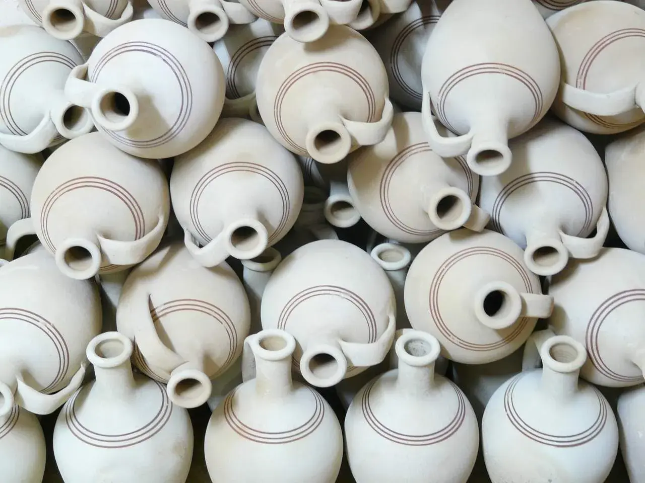 Un mucchio di giarre in terracotta, ognuna con un'ansa e due bocche, decorate con sottili linee marroni. Queste giarre, con il loro **giara significato** di contenimento e tradizione, creano un pattern visivo affascinante.