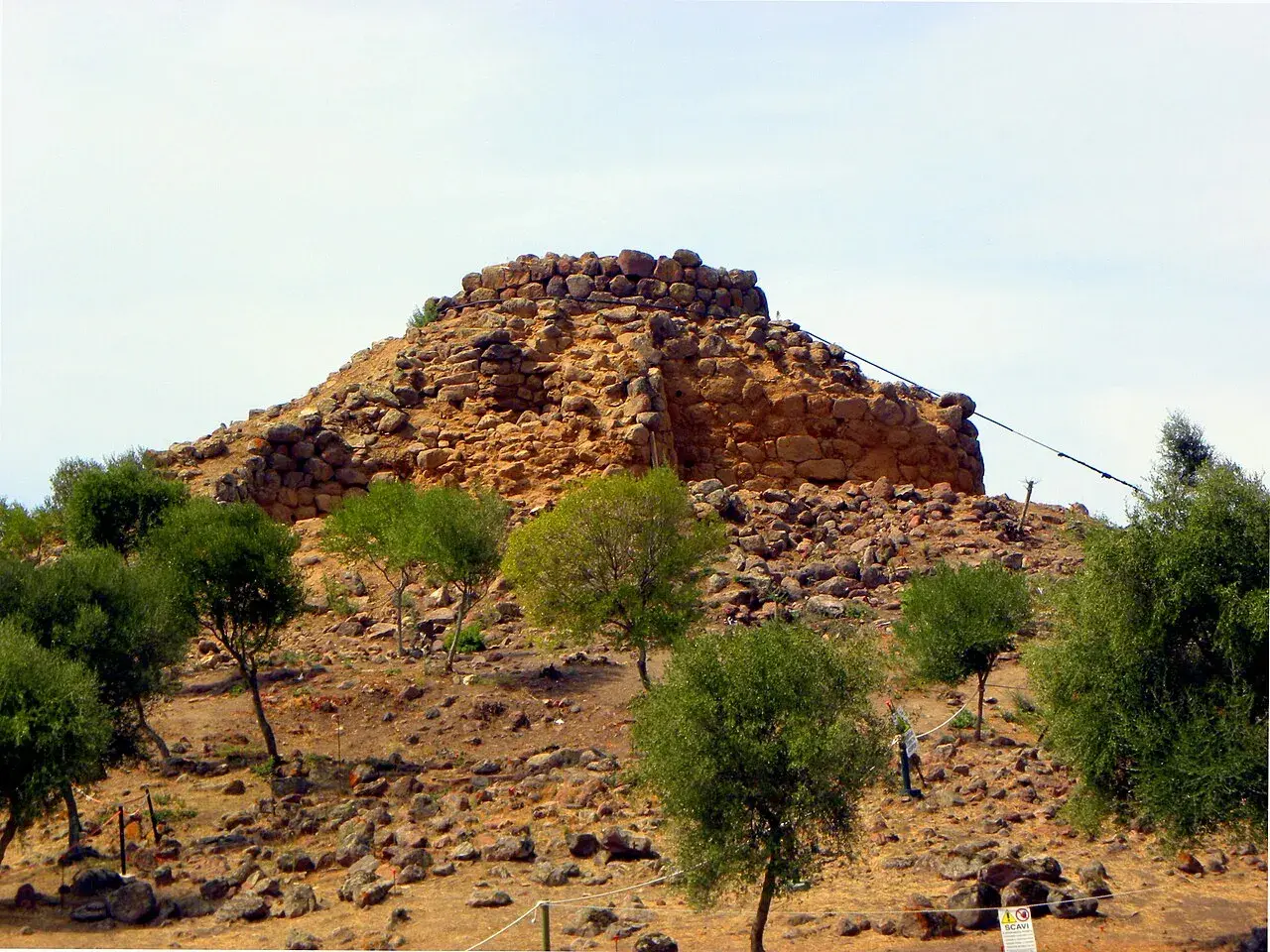 Il nuraghe Sirai, imponente struttura in pietra, si erge su un colle arido, circondato da vegetazione mediterranea.
