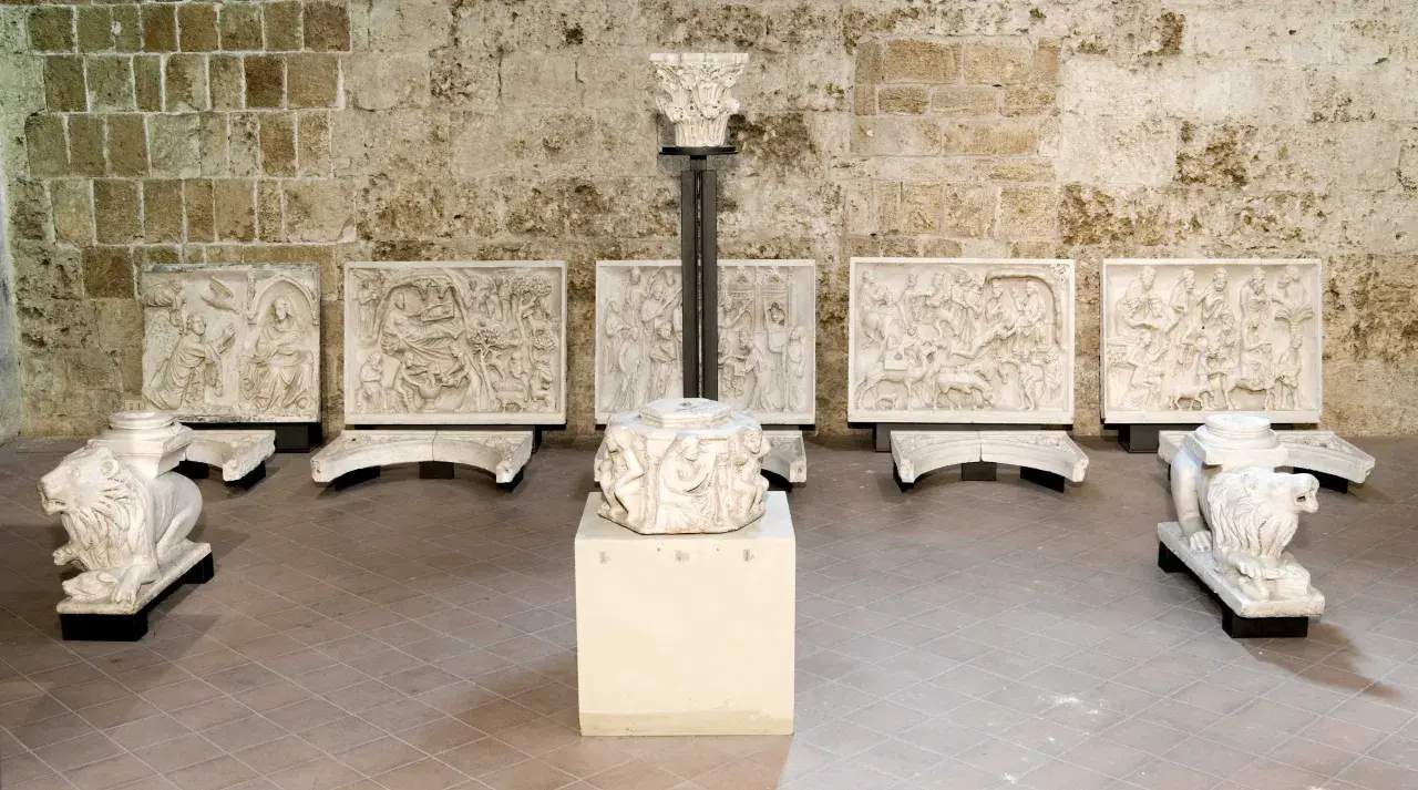 Sculture in pietra bianca, tra cui leoni stilofori e rilievi narrativi, forse frammenti di un antico pergamo, evocano un profondo significato storico e artistico.