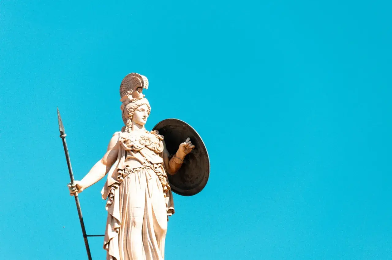 Statua di Atena, dea greca della giovinezza e della saggezza, con lancia e scudo contro un cielo azzurro.