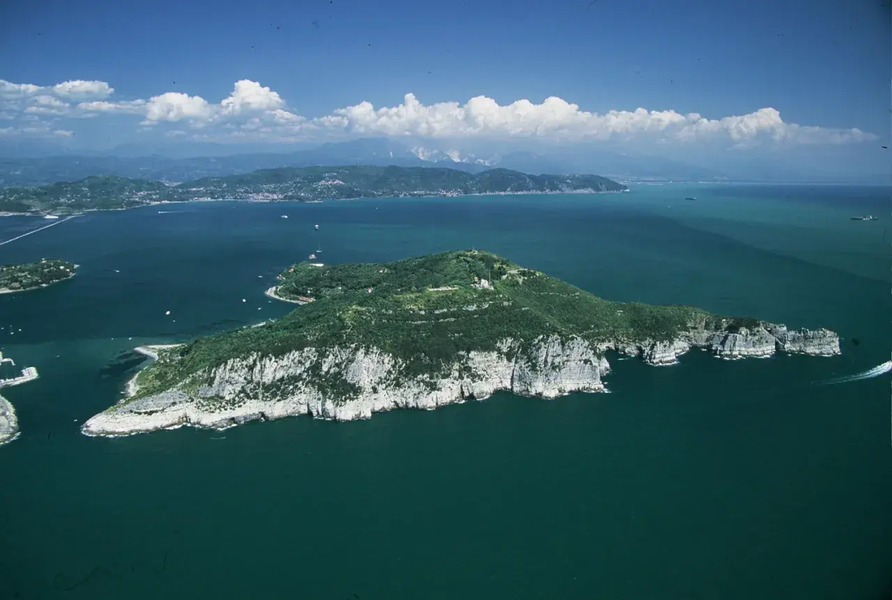 Isola verdeggiante con scogliere bianche, mare blu intenso e nuvole bianche. Si intravede la **grotta dei colombi** tra le rocce.