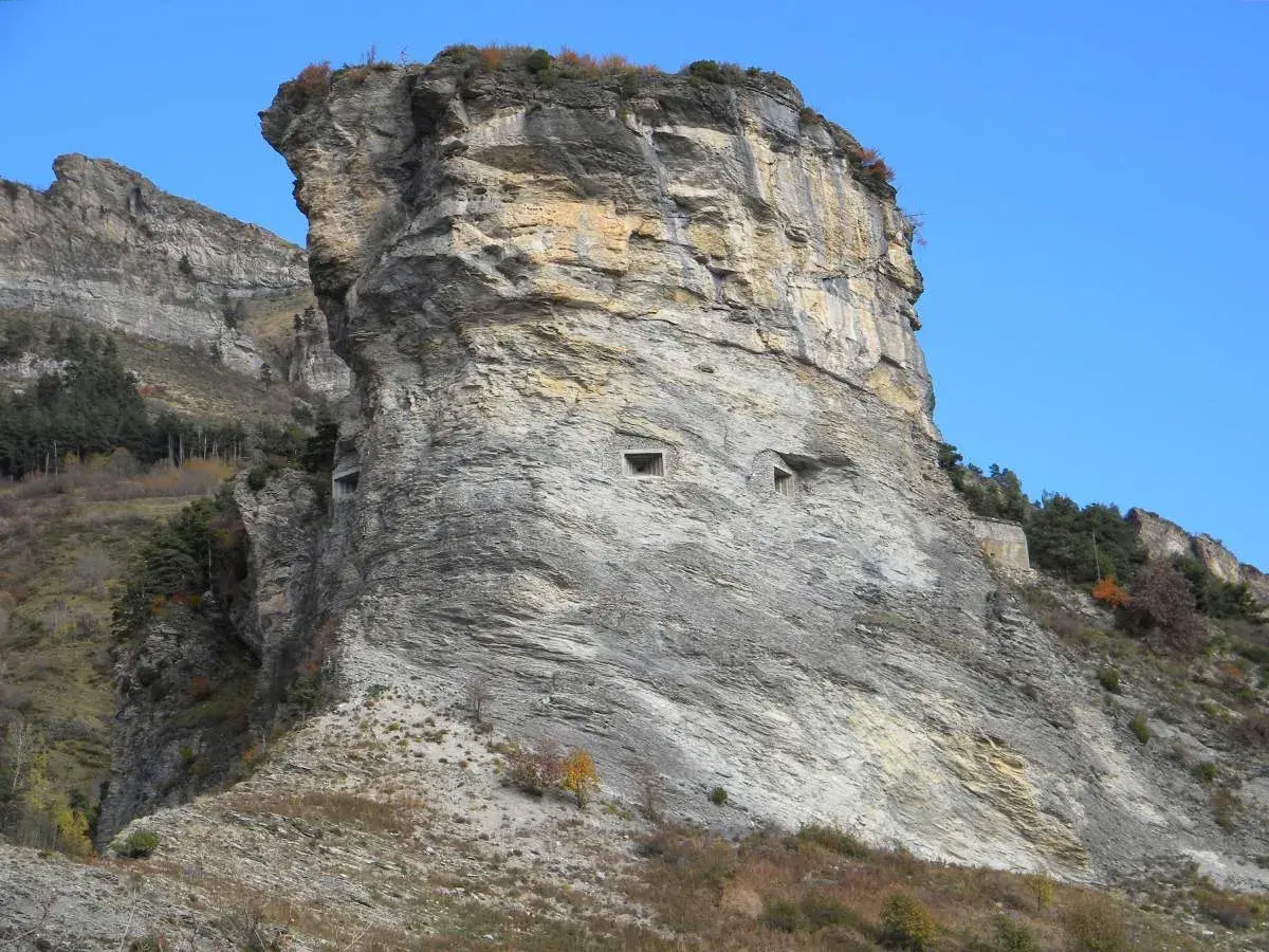 Imponente roccia con aperture che ricordano il vallo alpino del littorio. Un paesaggio montano suggestivo sotto un cielo azzurro.