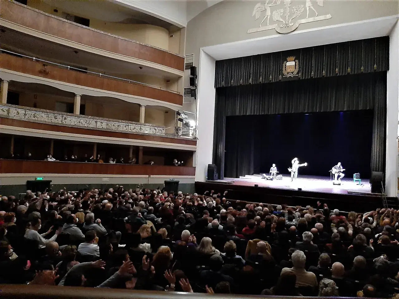 Un pubblico numeroso applaude sul palco, dove tre artisti si esibiscono in quello che potrebbe essere il primo teatro in Italia.