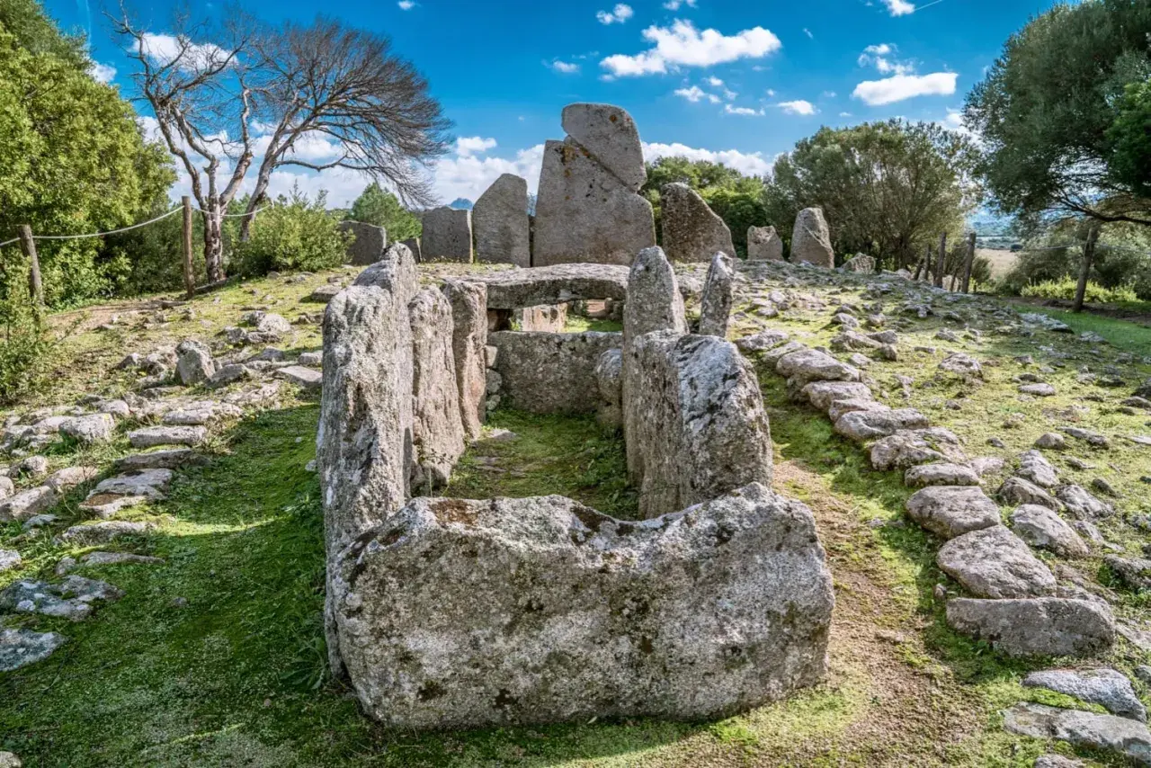 Antica tomba dei giganti di Li Lolghi, con imponenti pietre erette e un corridoio centrale, immersa nel verde sotto un cielo azzurro.