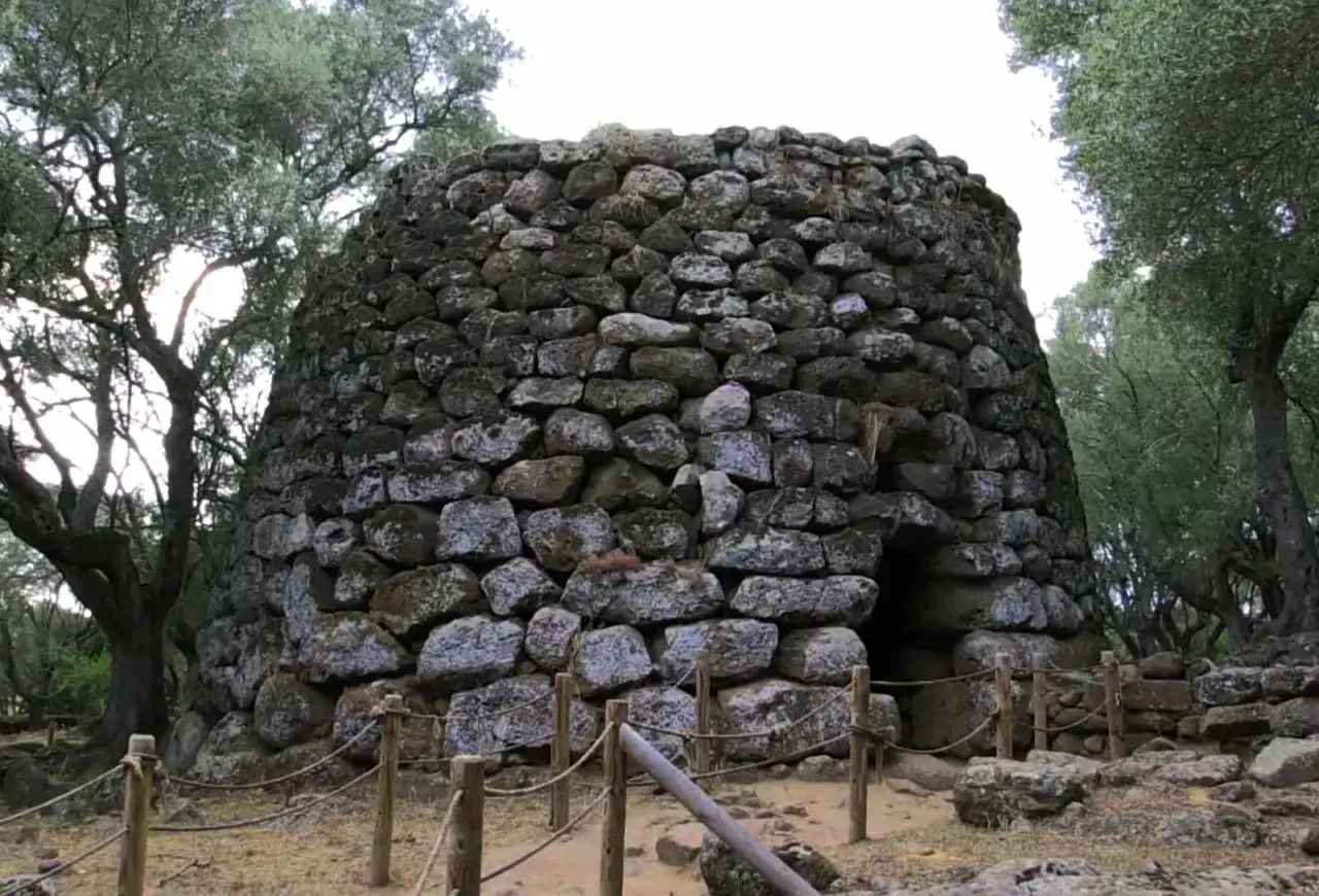 Antico nuraghe di Santa Cristina a Paulilatino, imponente struttura in pietra con un ingresso buio, circondato da alberi secolari.