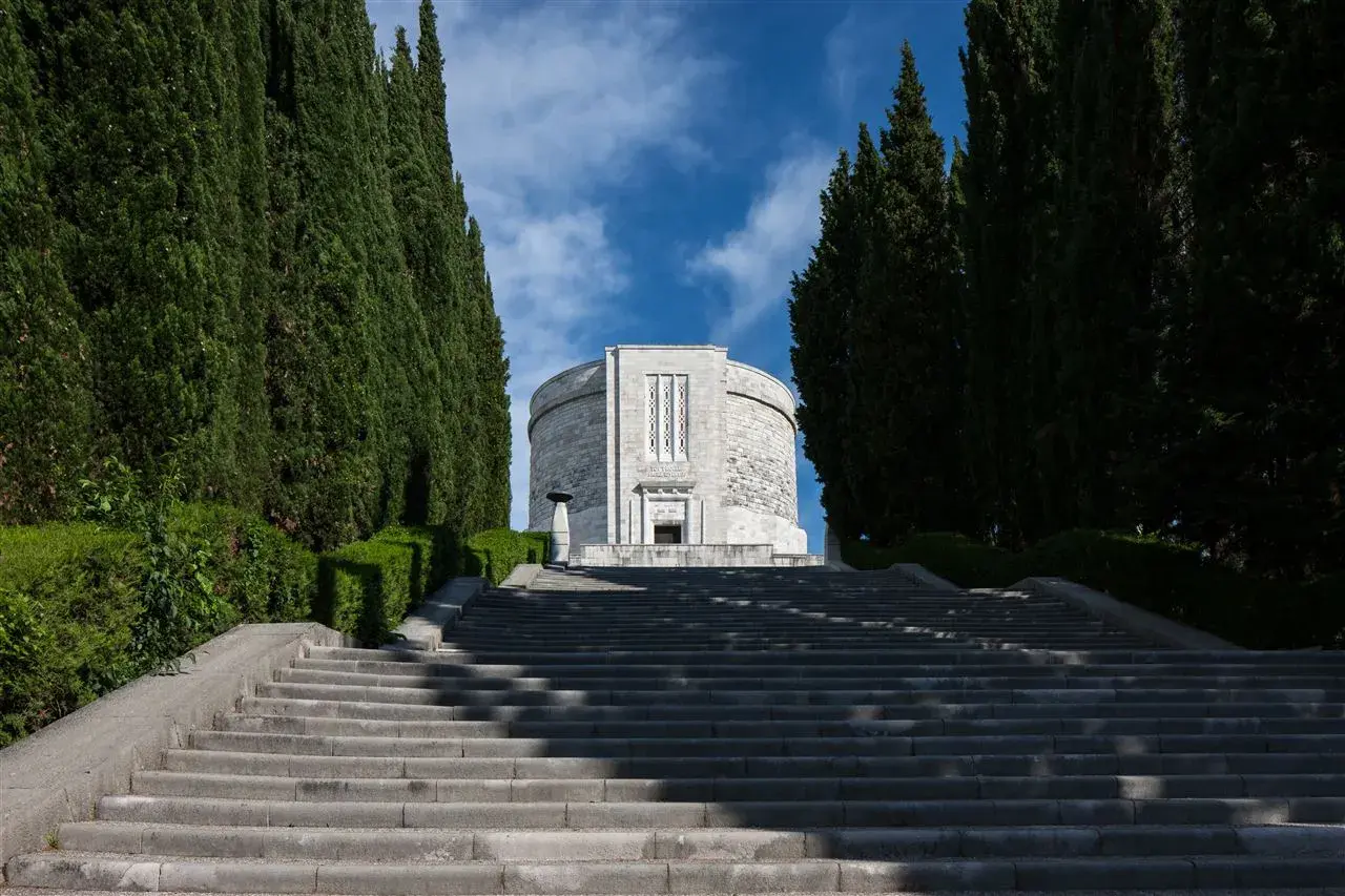 Lunga scalinata conduce all'imponente ossario di Oslavia, fiancheggiata da alti cipressi e vegetazione curata.