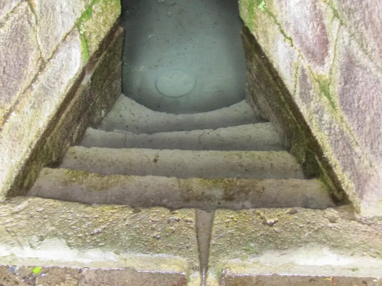 Antica scala in pietra conduce a un pozzo sacro in Sardegna, le cui acque limpide riflettono il cielo.