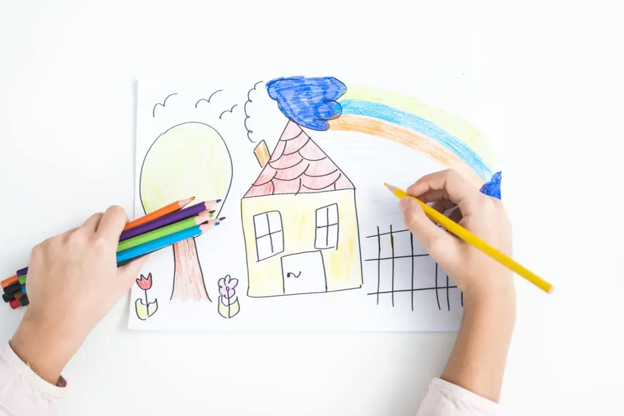 Bambino colora un disegno con matite, creando una casa, un albero e un arcobaleno. La dea Ebe, simbolo di giovinezza, ispira la creatività.