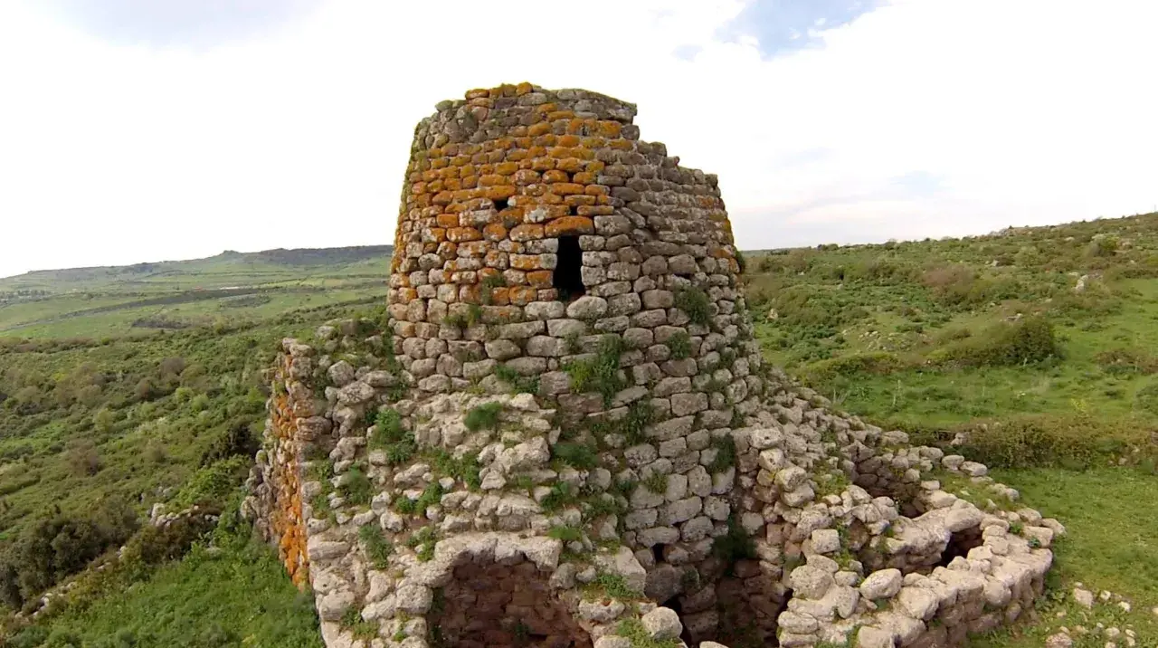 Il nuraghe Santa Barbara, con la sua torre in pietra ricoperta di licheni arancioni, domina un paesaggio verdeggiante e collinare.