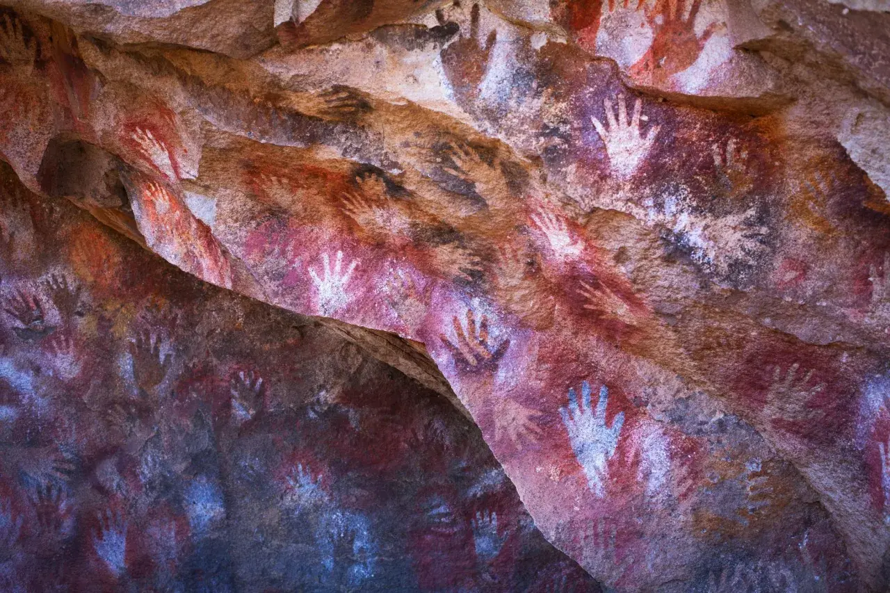 Antiche pitture rupestri nella grotta delle mani, con impronte di mani rosse e bianche su roccia.