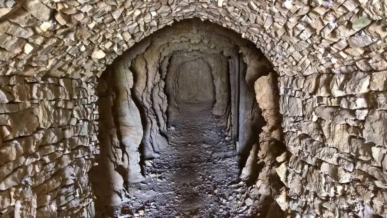 Un tunnel scavato nella roccia, con pareti in pietra grezza e un soffitto a volta. Un luogo che evoca il ricordo dei caduti della Prima Guerra Mondiale.