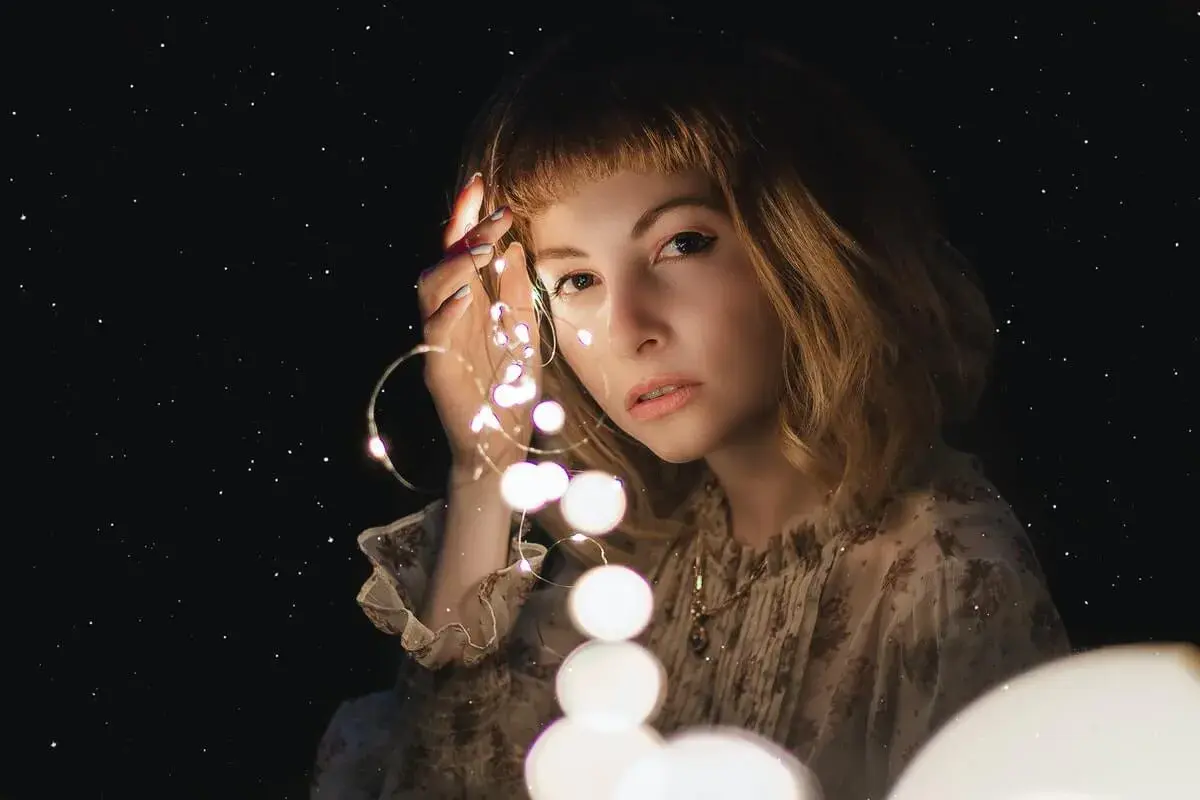 Una ragazza con luci scintillanti tra le dita, come un filo di Arianna che illumina il buio.