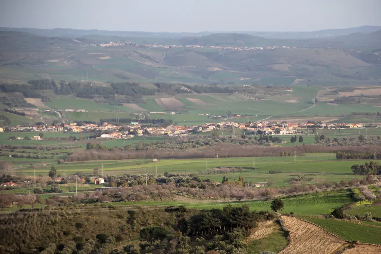 Paesaggio collinare con campi coltivati e case sparse, in lontananza si intravede il borgo di Pauli Arbarei, Sardegna.