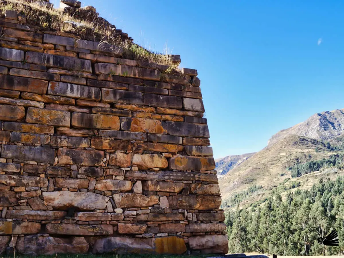 Antiche mura di pietra a Chavin de Huantar, con montagne verdi e cielo azzurro sullo sfondo.