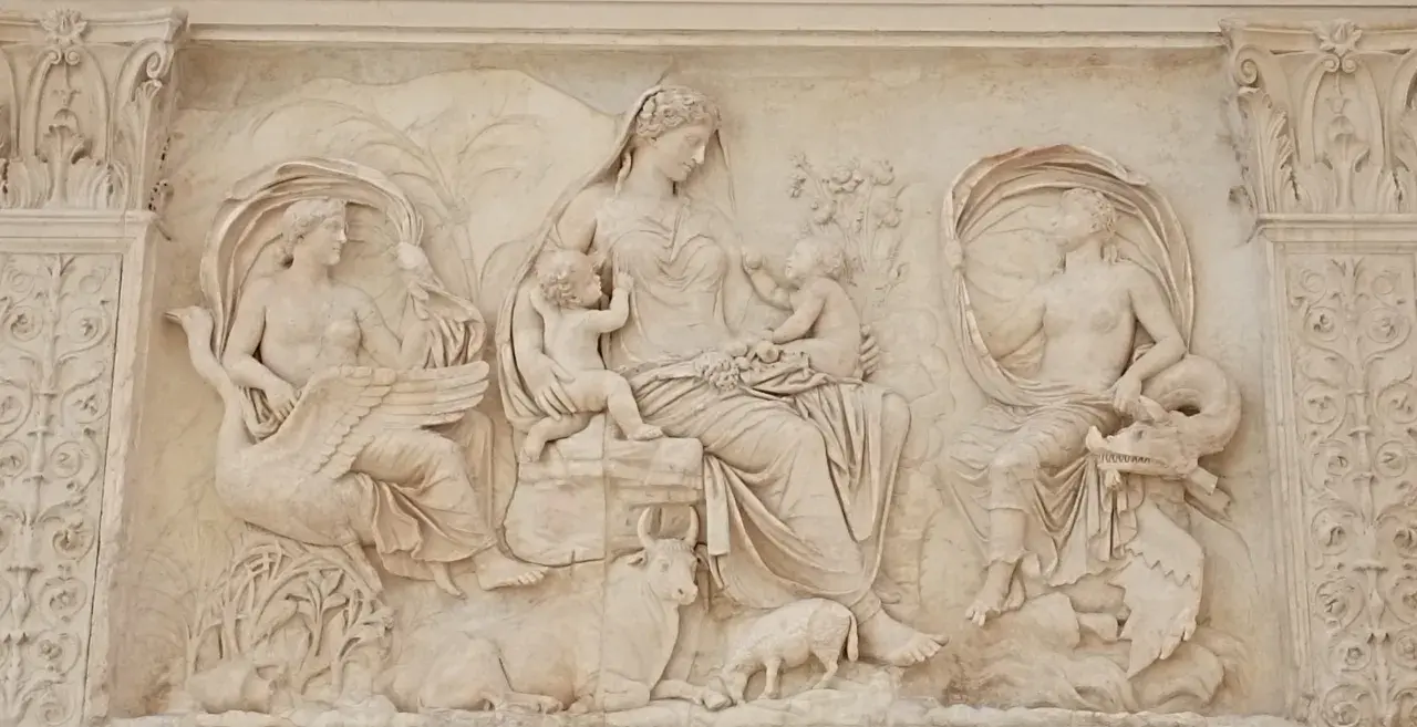 Rilievo esterno dell'Ara Pacis: una madre con due bambini, affiancata da figure femminili con cigno e creatura marina, circondata da animali e vegetazione.