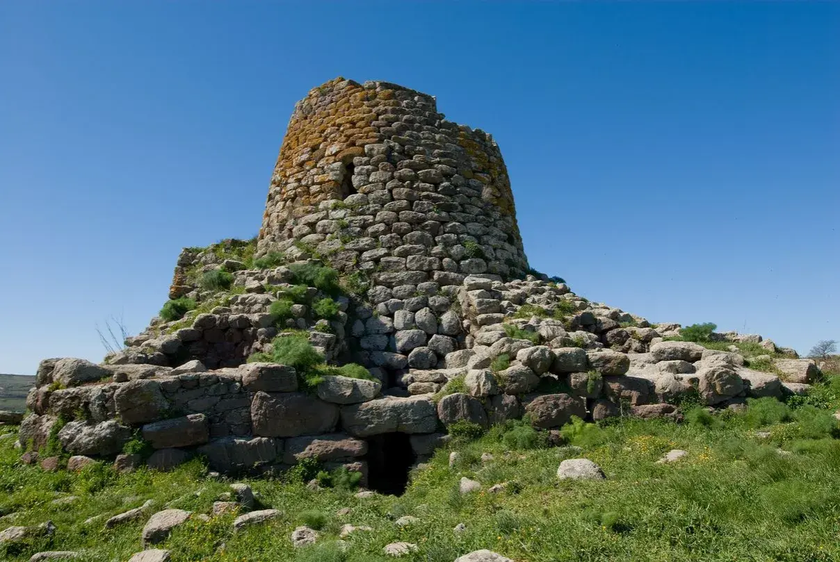 Il nuraghe Santa Barbara a Villanova Truschedu, imponente struttura in pietra con vegetazione rigogliosa, si erge sotto un cielo azzurro.