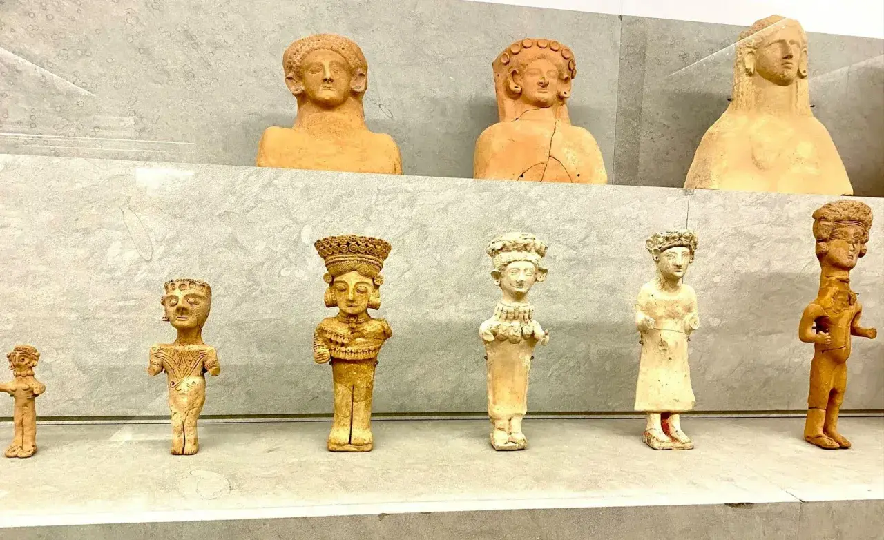 Antiche statuette in terracotta, tra cui una dea punica della fertilità, esposte su una mensola.