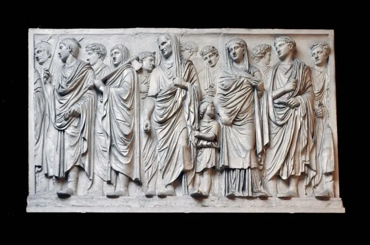 Rilievo in marmo dell'Ara Pacis di Augusto: una processione di figure romane, uomini, donne e bambini, con toghe drappeggiate.