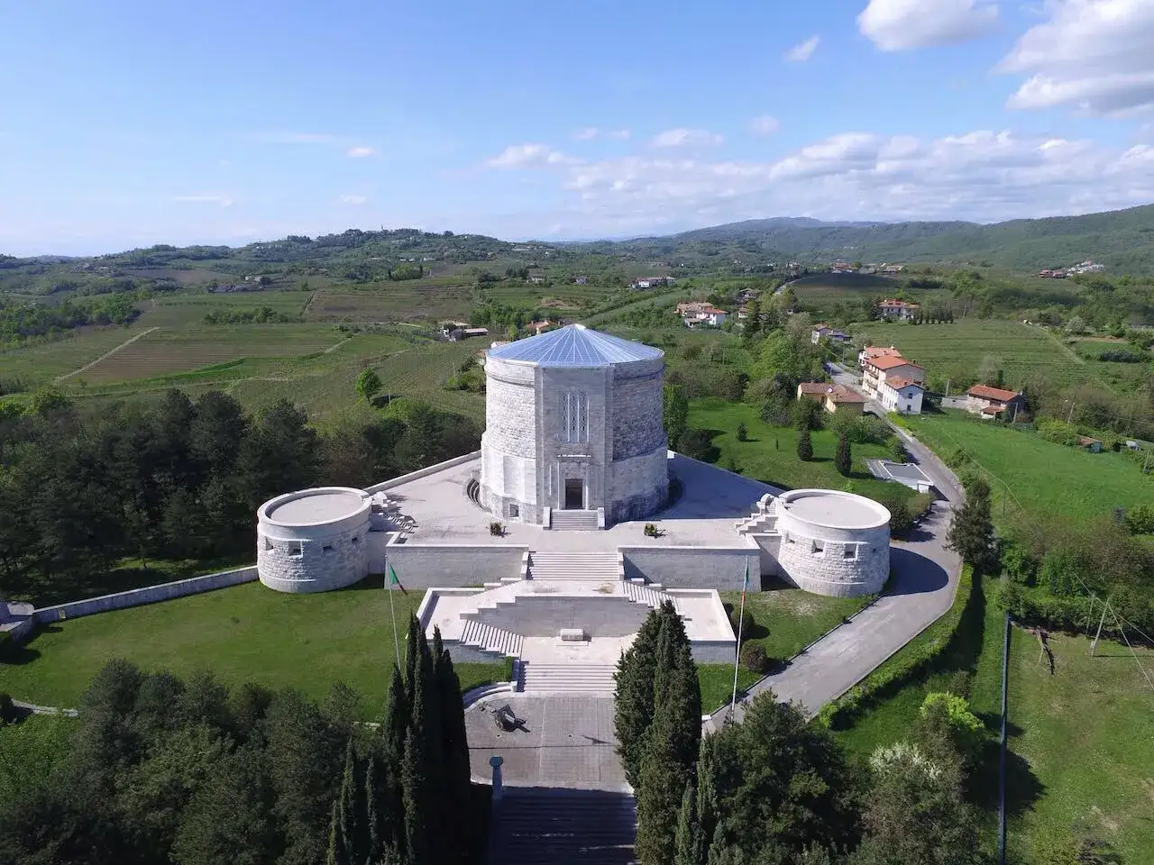L'imponente ossario di Oslavia, con le sue torri circolari, domina un paesaggio collinare verdeggiante, tra vigneti e case sparse.