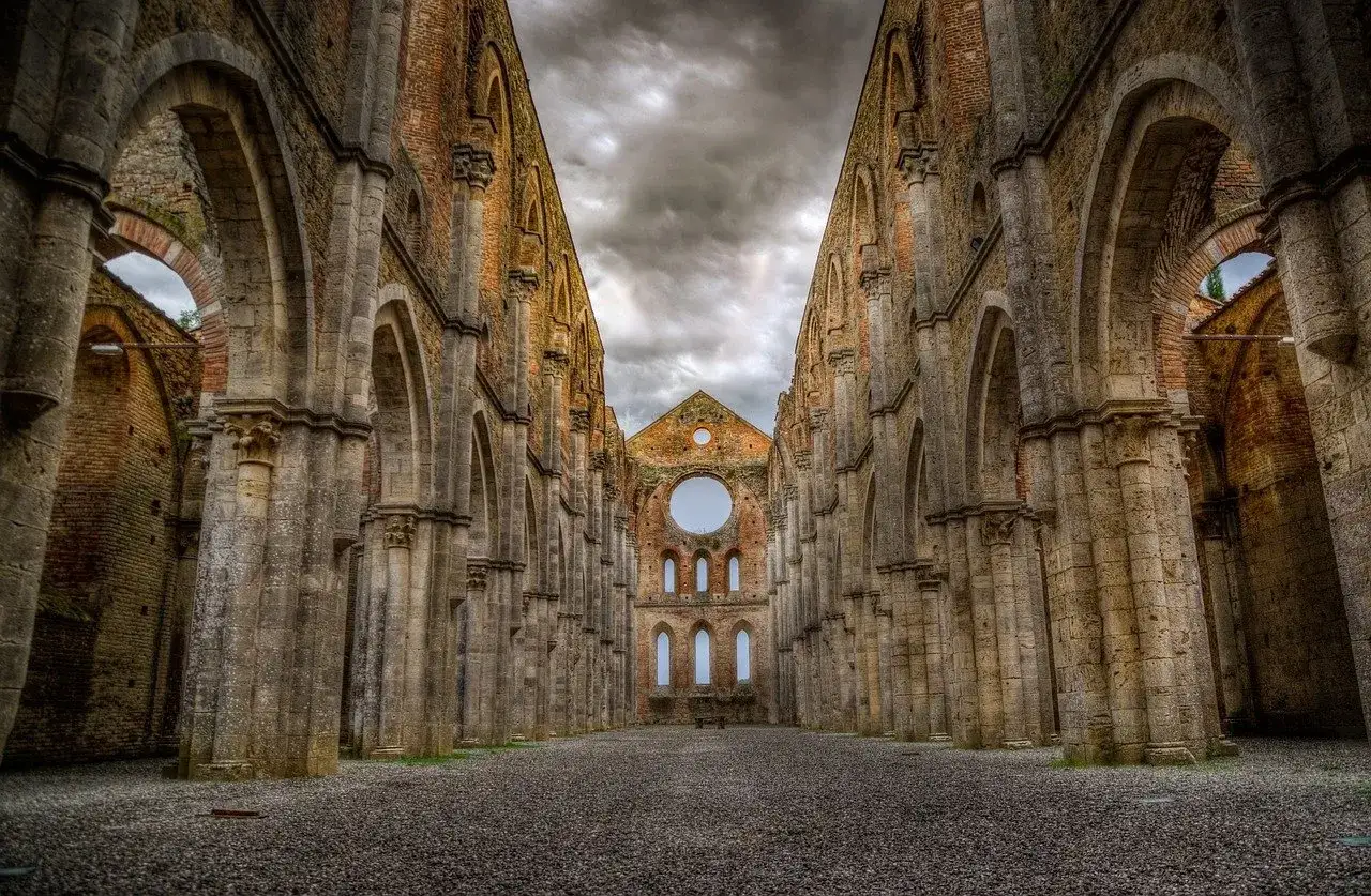 L'imponente abbazia nel querceto, con le sue arcate maestose e il tetto mancante, si staglia contro un cielo tempestoso, evocando un senso di storia e mistero.
