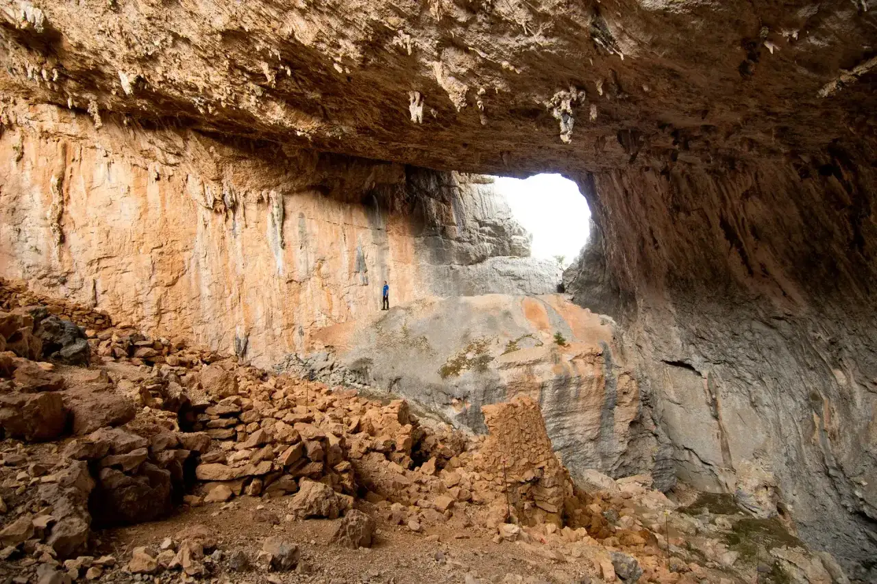 Un uomo in piedi in un'enorme grotta, un sito archeologico di Tiscali, con rocce e stalattiti.